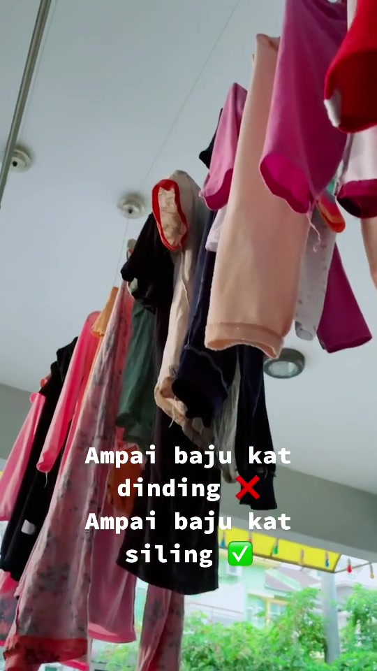 Pandangan mendongak ke arah baju berwarna-warni bergantung pada penyangkut di palang yang digantung dari siling koridor terbuka