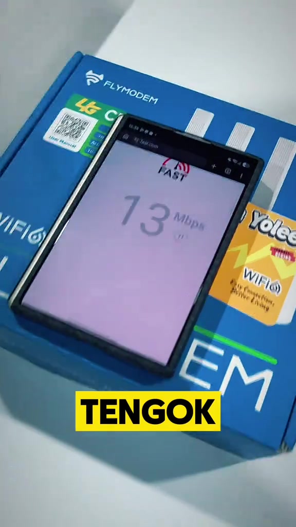 Telefon menjalankan speedtest di atas kotak biru FlyModem menunjukkan keputusan 13 Mbps pada rangkaian 4G