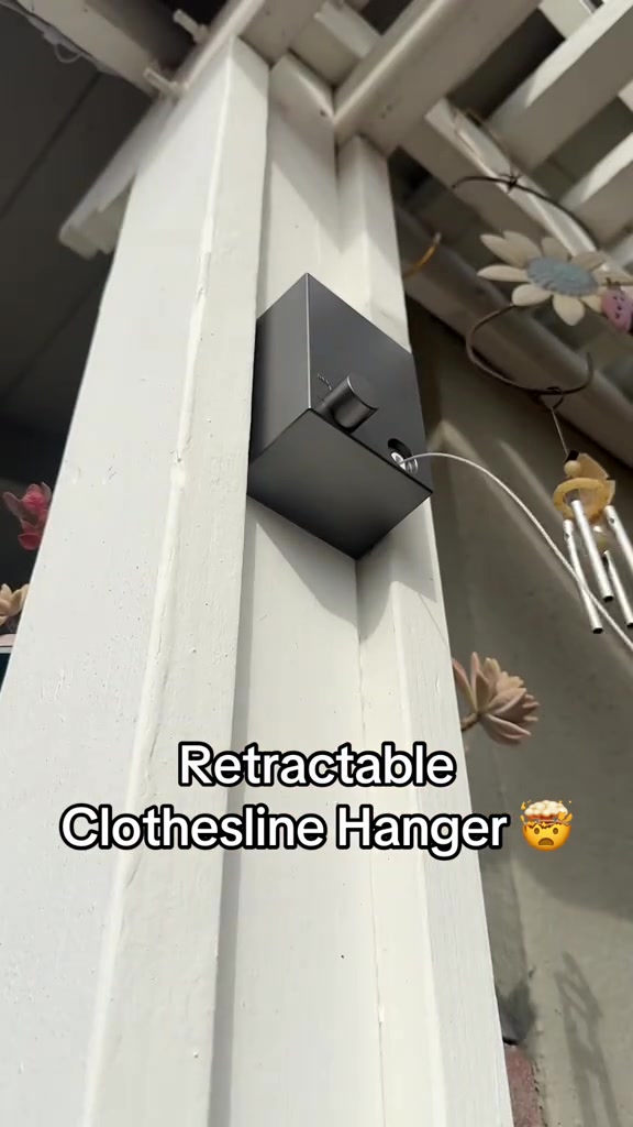 Kotak retractable clothesline kelabu dipasang pada tiang porch putih dengan loceng angin bergantung di sebelahnya