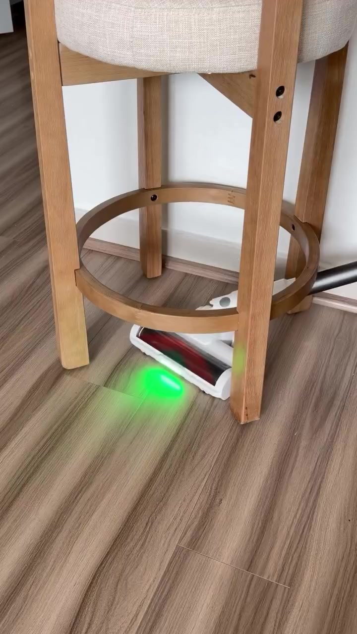 Kepala vacuum cordless dengan lampu hijau masuk ke bawah kaki stool kayu atas lantai vinyl motif kayu
