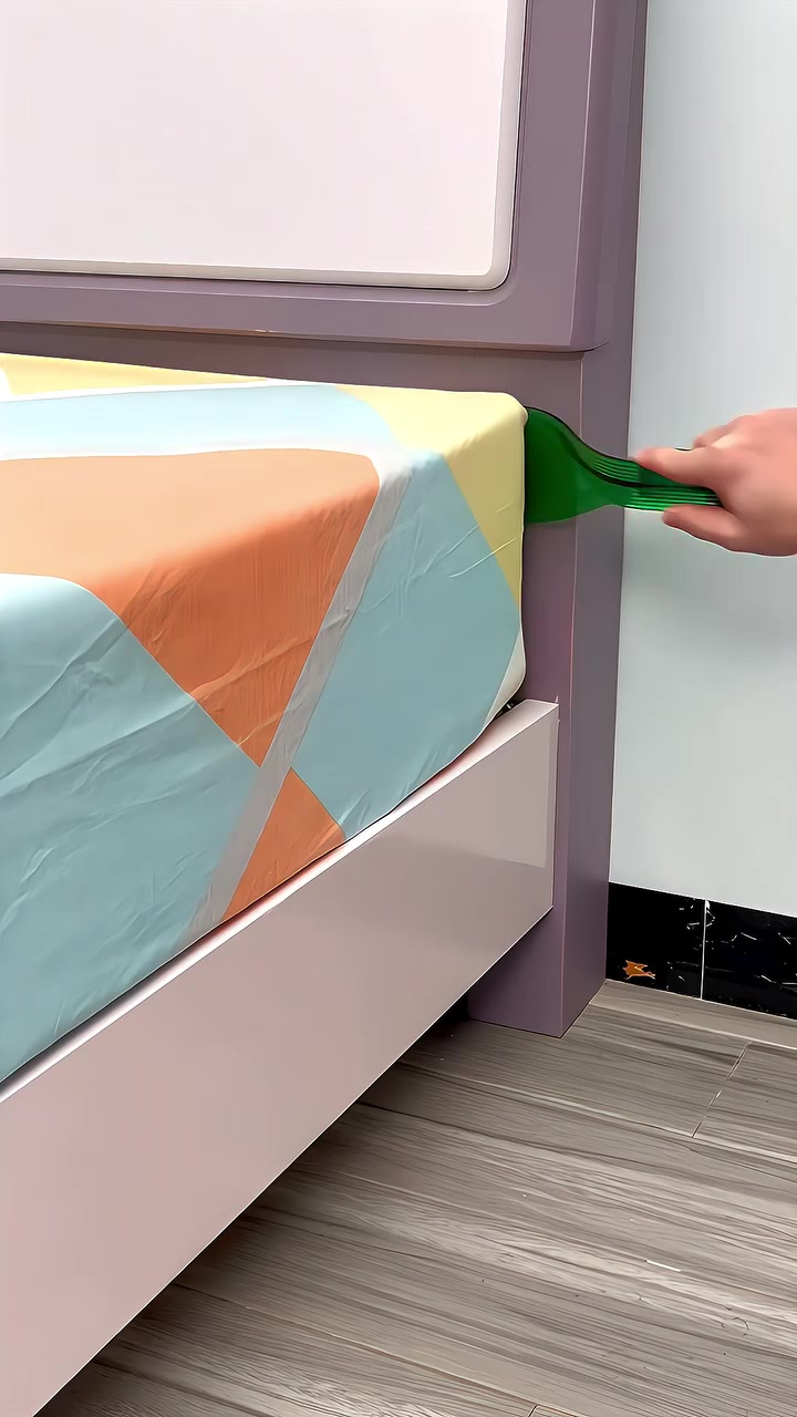 Tangan memegang alat bed sheet tucker hijau di penjuru katil, menolak cadar ke bawah tilam