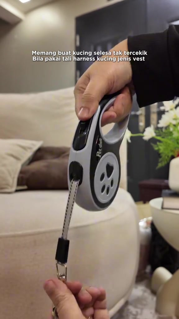 Pemegang tali kucing jenis retractable kelabu hitam dengan motif tapak kaki, dipegang di ruang tamu