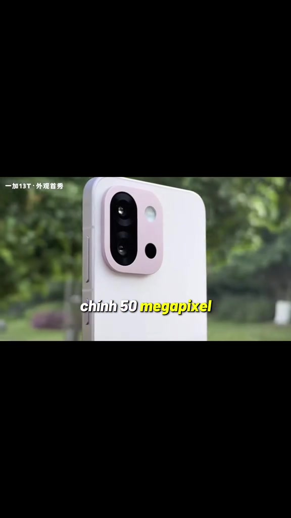 Cụm camera OnePlus 13T màu hồng nhạt với hai ống kính xếp dọc và đèn flash tròn, nền cây xanh ngoài trời