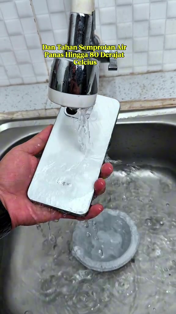 Belakang phone putih dibilas bawah air paip yang mengalir di singki, dengan teks video menyatakan ia tahan semburan air panas hingga 80 darjah Celsius