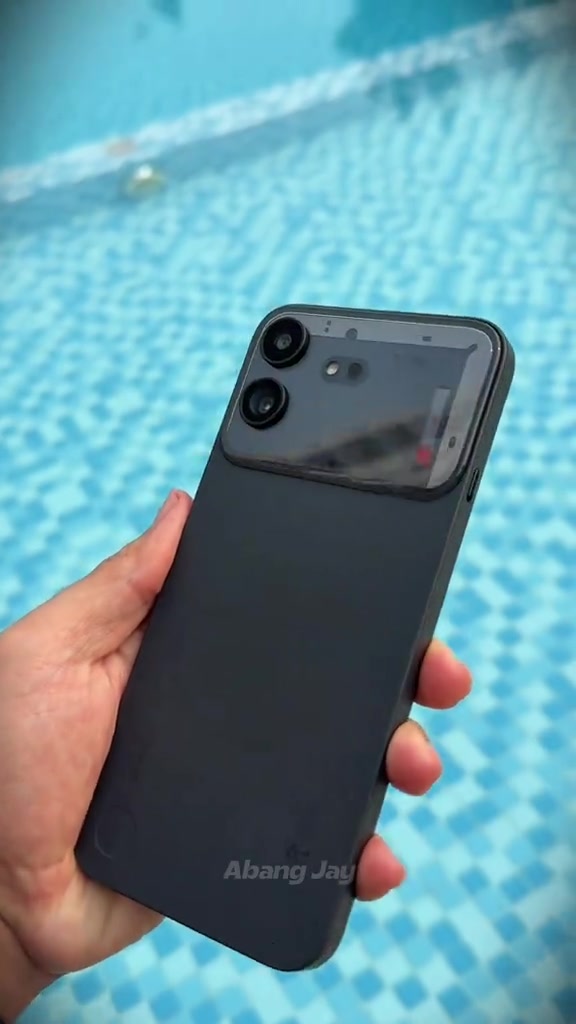 Nothing Phone (4b) warna hitam dipegang sebelah tangan dengan latar kolam renang biru, nampak panel transparent di bahagian atas belakang
