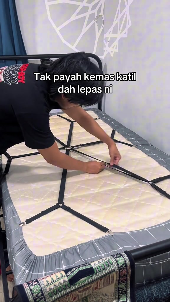 Orang memasang strap elastik hitam bersilang di bawah tilam katil single untuk memegang penjuru cadar