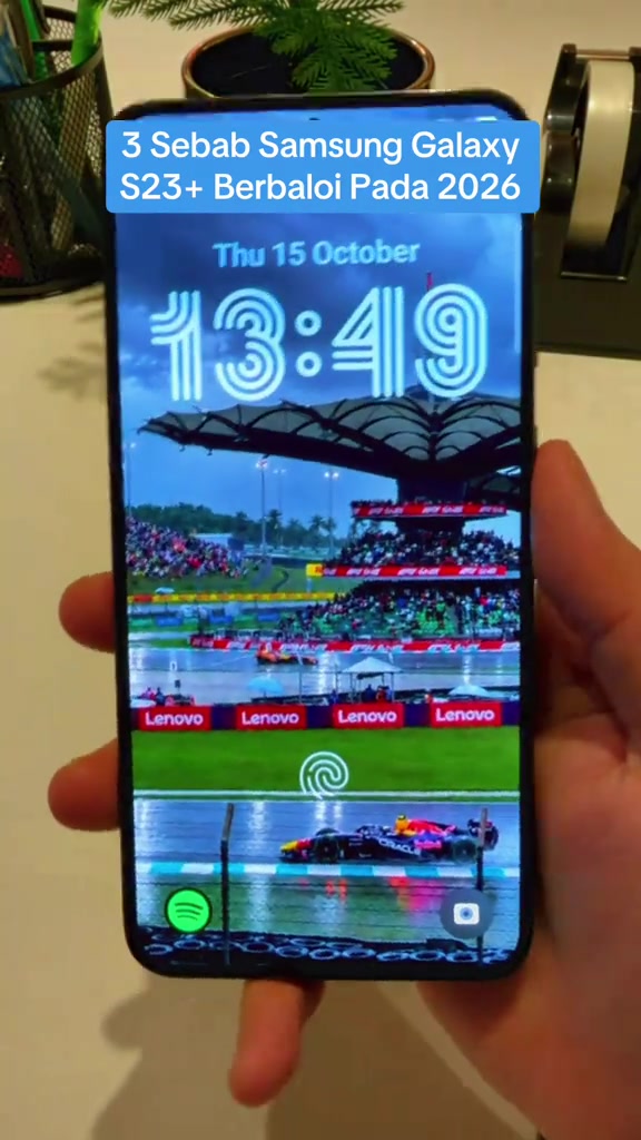 Skrin depan Samsung Galaxy S23+ papar skrin kunci dengan wallpaper litar perlumbaan, dipegang dengan satu tangan