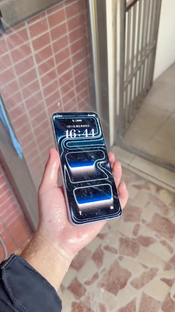 Tangan basah memegang phone bertitik air dengan skrin masih menyala menunjukkan jam selepas ujian rendaman air