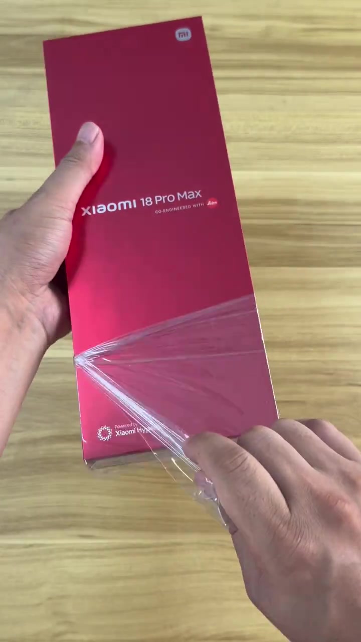 Kotak merah Xiaomi 18 Pro Max sedang dibuka balutan plastiknya di atas meja kayu