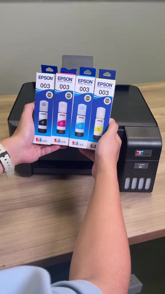 Dua tangan memegang empat kotak dakwat botol Epson 003 di hadapan printer EcoTank L3250 berwarna hitam