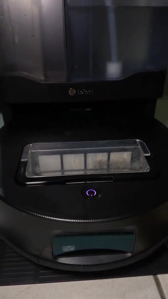 Robot vacuum hitam berhenti di dock stesen sendiri dengan bekas habuk lutsinar kelihatan dari atas