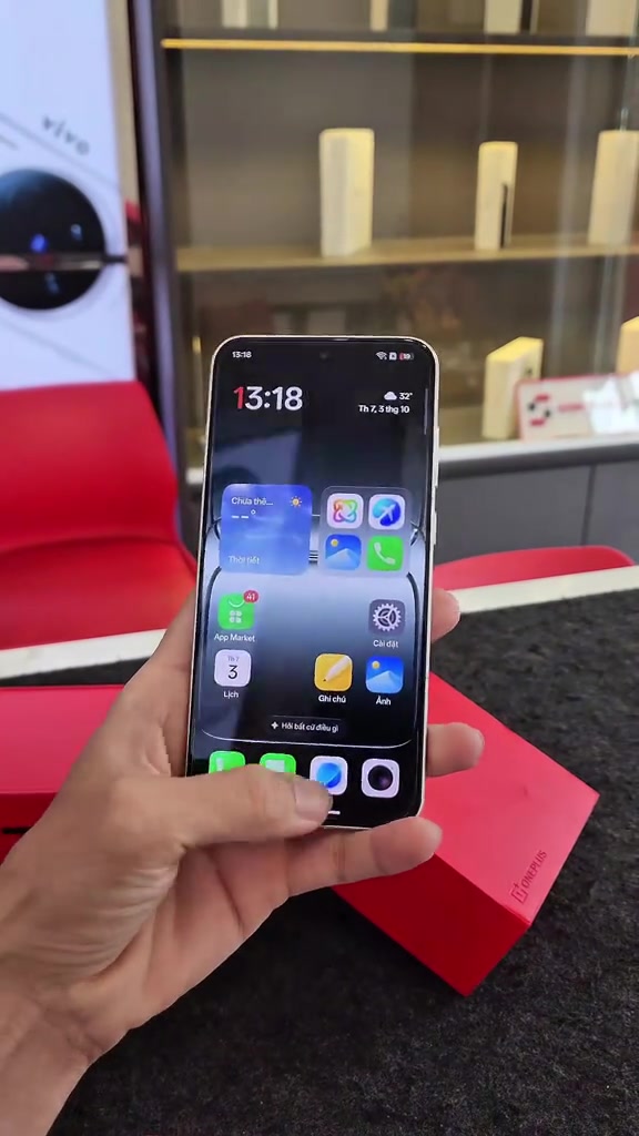 Mặt trước OnePlus 13T cầm trên tay trong cửa hàng, màn hình home hiện giao diện tiếng Việt với các icon App Market, Cài đặt, Ghi chú