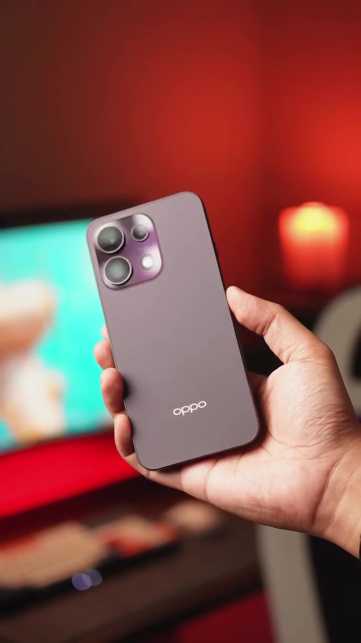 Seluruh badan belakang OPPO Reno16 F 5G warna ungu dipegang satu tangan dengan latar merah kabur