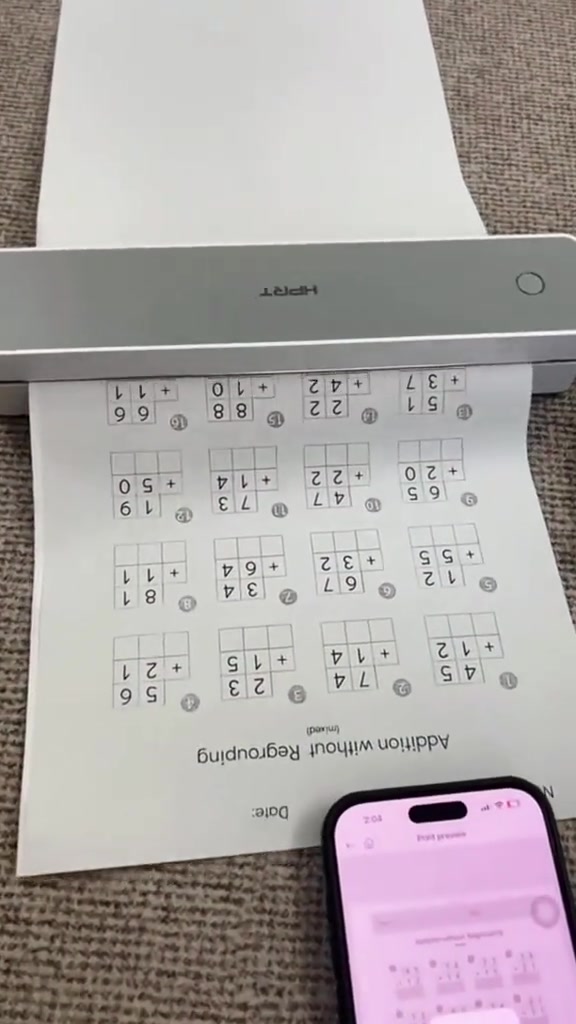 Printer thermal HPRT berwarna kelabu sedang mencetak helaian latihan bertulis, dengan telefon pintar di sebelahnya