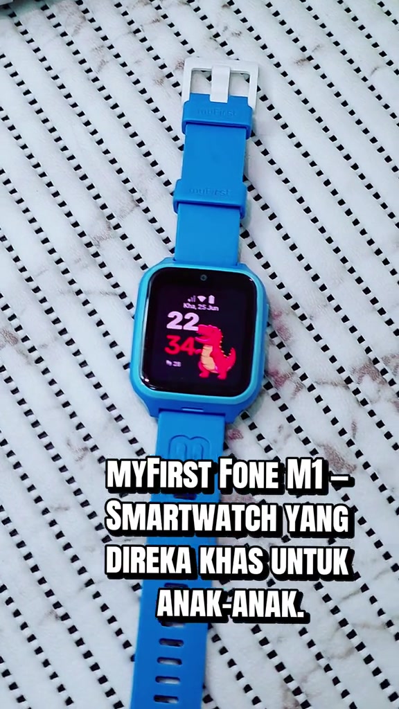 myFirst Fone M1 biru dibaringkan rata, skrin menyala dengan muka jam dinosaur