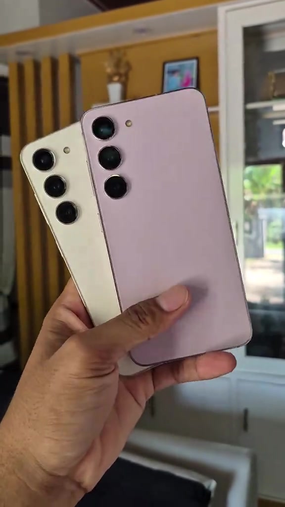 Dua unit Samsung Galaxy S23 terpakai warna lavender dan krim dipegang serentak, nampak tiga modul kamera belakang