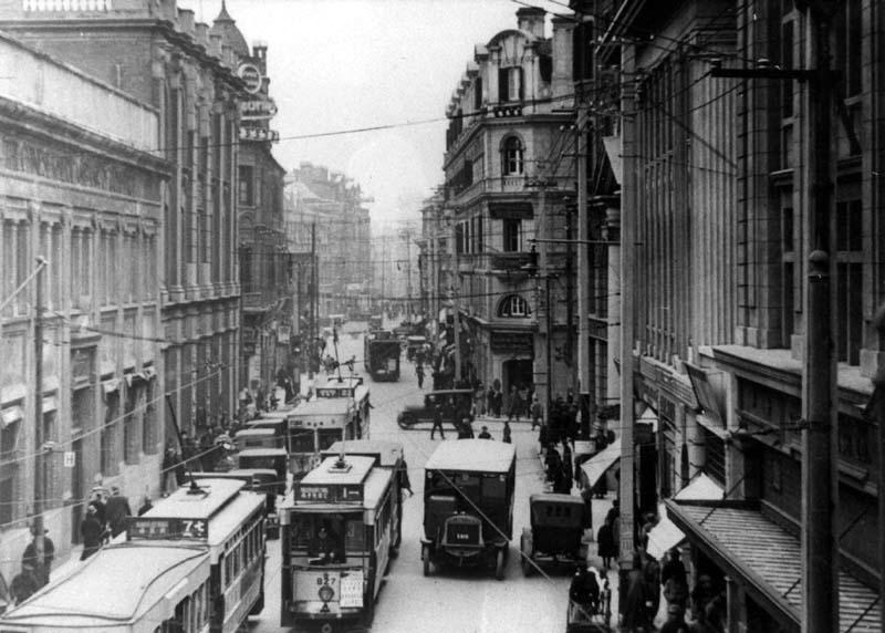 Phố Thượng Hải thập niên 1920 đen trắng với dãy tàu điện chạy giữa lòng đường và người đi bộ nhỏ xa phía xa