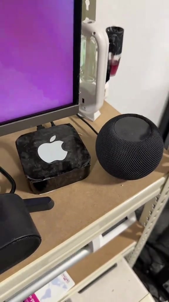 Unit Apple TV bersebelahan speaker HomePod mini di atas meja di sebelah monitor