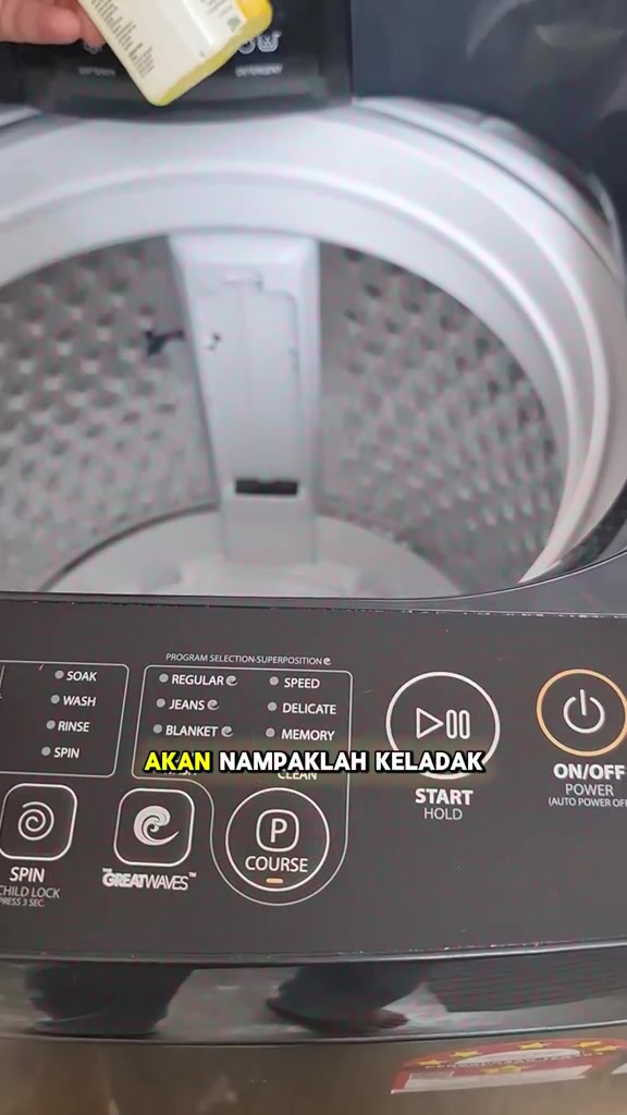 Tangan menuang cecair pembersih mesin basuh ke dalam drum kosong di hadapan panel kawalan