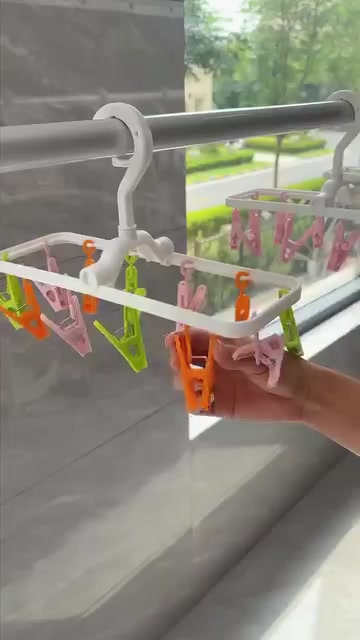 Hanger lipat berklip warna putih dengan klip hijau, oren dan pink tergantung pada rail besi dekat tingkap