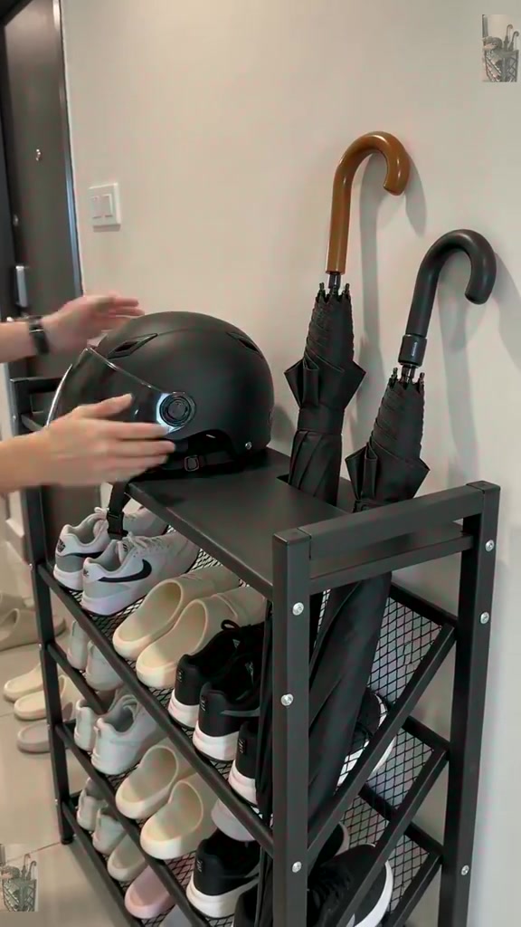 Rak kasut besi hitam di pintu masuk rumah dengan topi keledar di atas dan dua payung dalam slot sisi