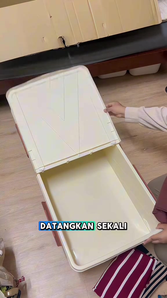 Tangan membuka penutup kotak simpanan plastik krim berbentuk panjang di lantai