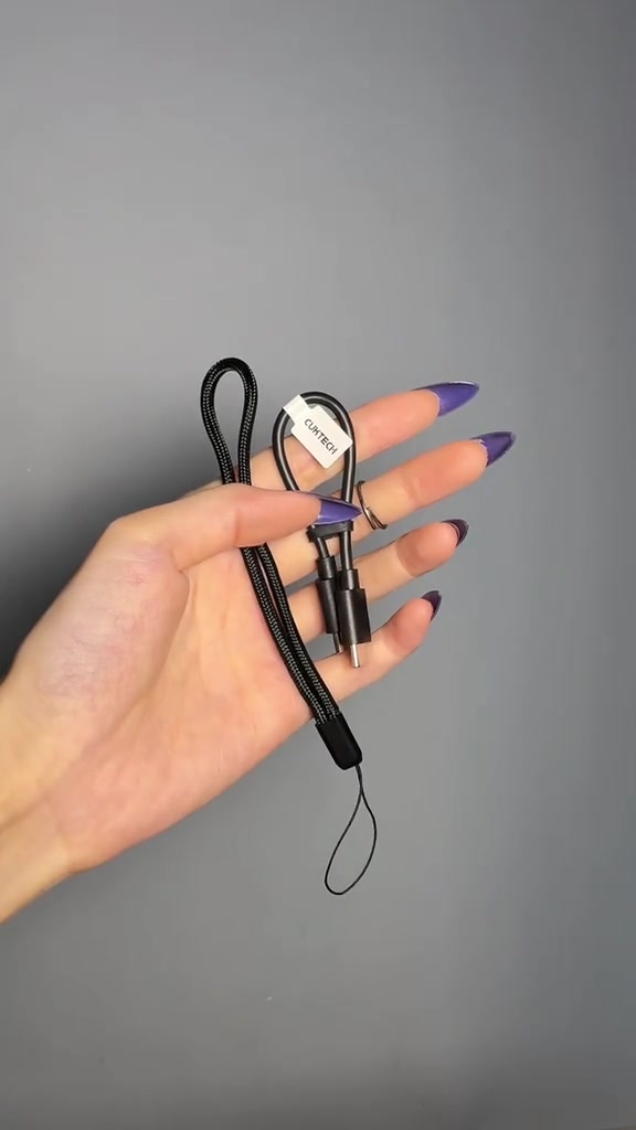 Bàn tay cầm sợi cáp liền đầu USB-C dài 15 cm và dây đeo dạng dù của CUKTECH 10 mini trên nền xám