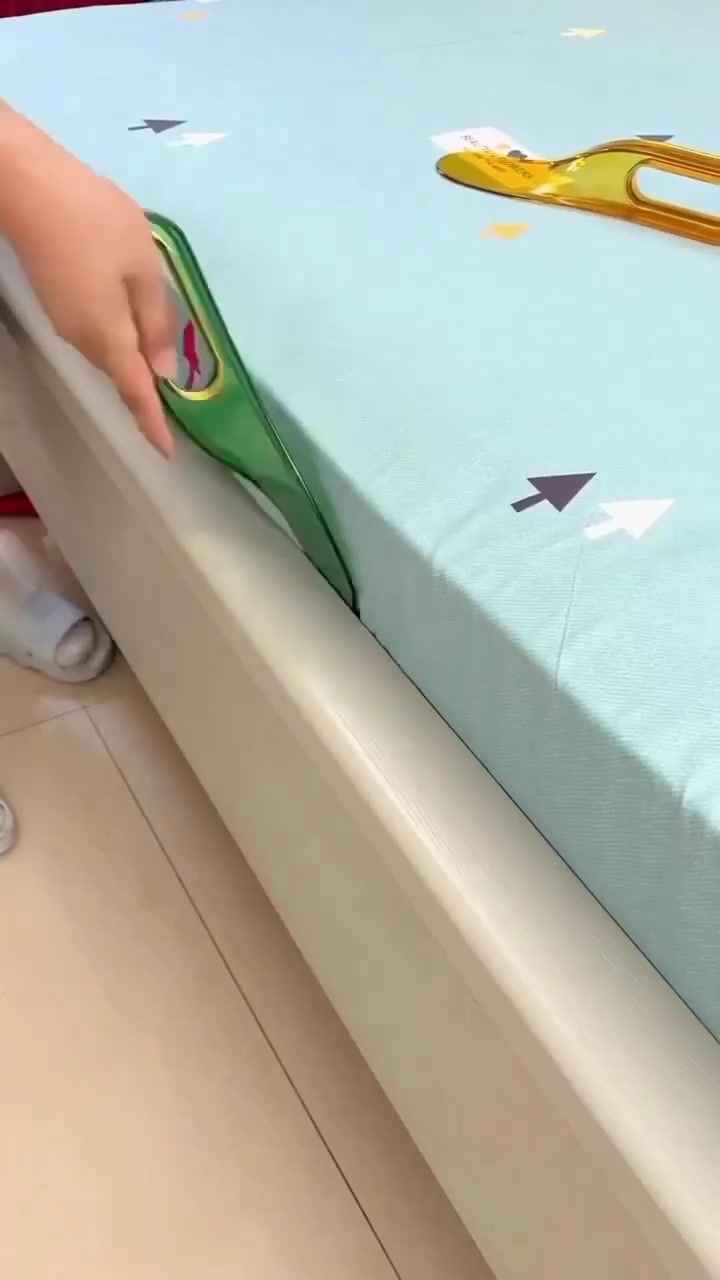 Alat bed sheet tucker hijau diselitkan tegak ke celah antara tilam dan rangka katil untuk mengangkat tepi tilam