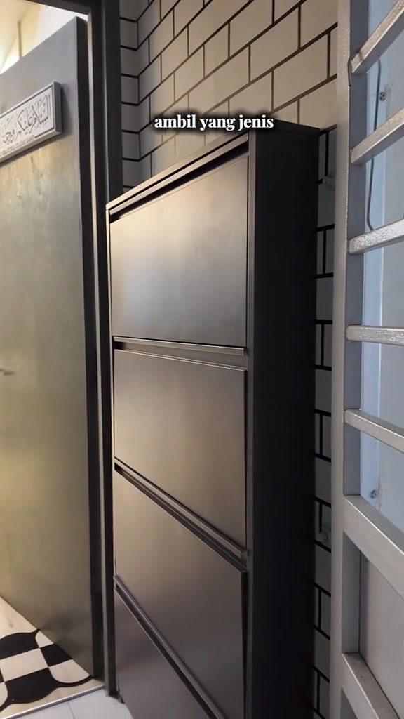 Kabinet kasut slim berwarna hitam diletak di ruang sempit antara pintu utama dan jerjak rumah