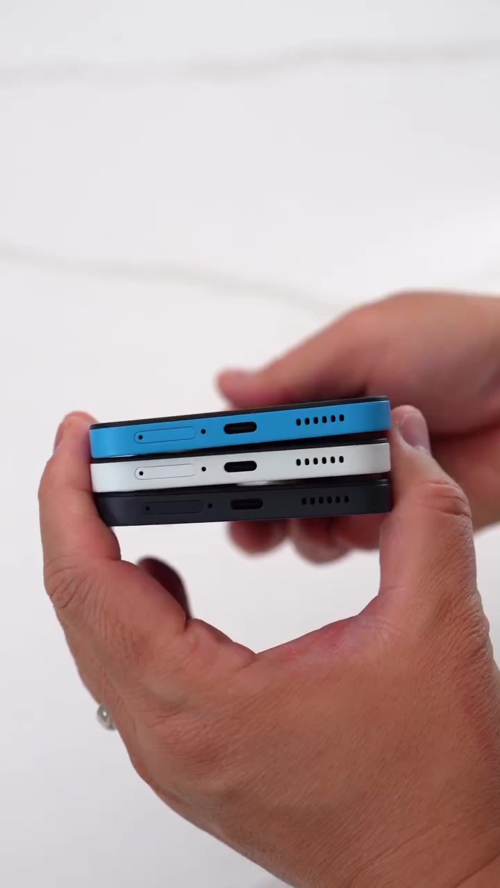 Tiga unit Nothing Phone (4b) warna biru, putih dan hitam bertindan, nampak port USB-C dan gril speaker di bahagian bawah