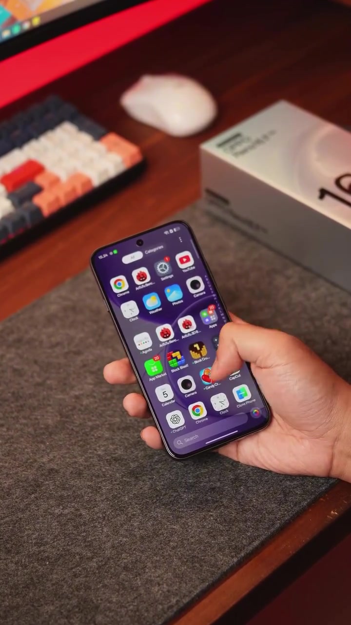 Skrin depan OPPO Reno16 F 5G menyala dengan deretan ikon aplikasi, dipegang satu tangan di atas meja kerja