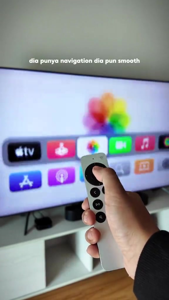 Tangan memegang Siri Remote menghadap skrin TV yang memaparkan halaman utama tvOS