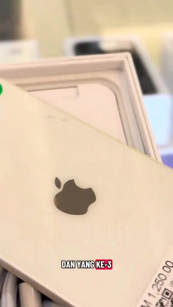 Bahagian belakang iPhone warna putih emas di atas kotak dengan tag harga kedai bercetak RM1,250.00 kelihatan separuh di penjuru bawah