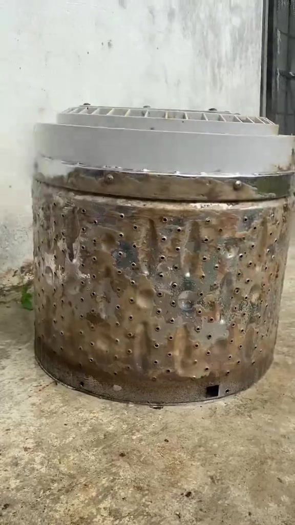 Drum stainless mesin basuh berdiri di lantai dengan dinding luar berkerak perang tebal selepas dikeluarkan