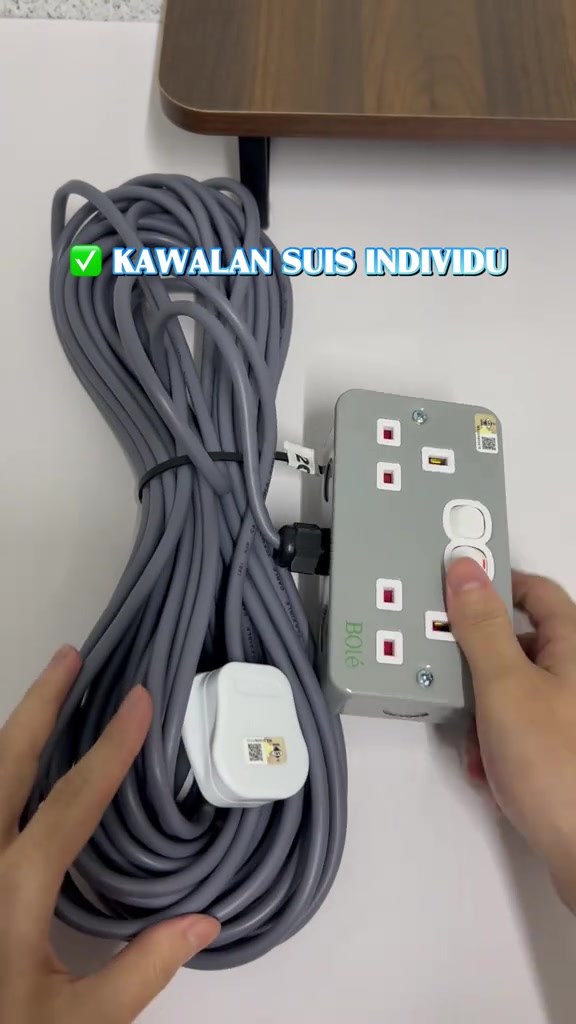 Kotak soket extension besi kelabu dengan empat soket dan suis individu putih, wayar kelabu bergulung di sebelah dan plug putih berhampiran