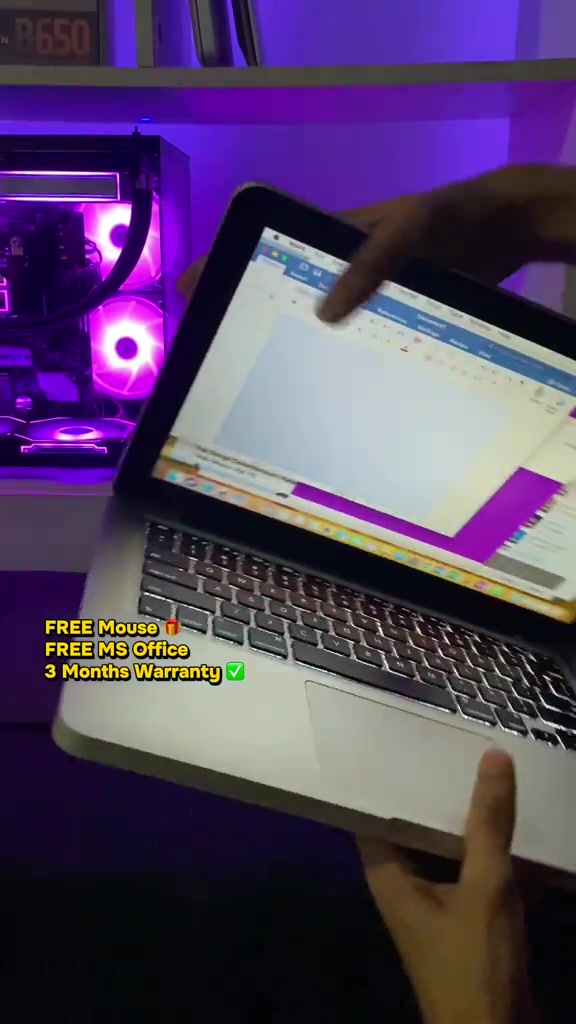 MacBook Pro perak terbuka dipegang tangan, teks pada bingkai menyebut free mouse, free MS Office dan waranti 3 bulan