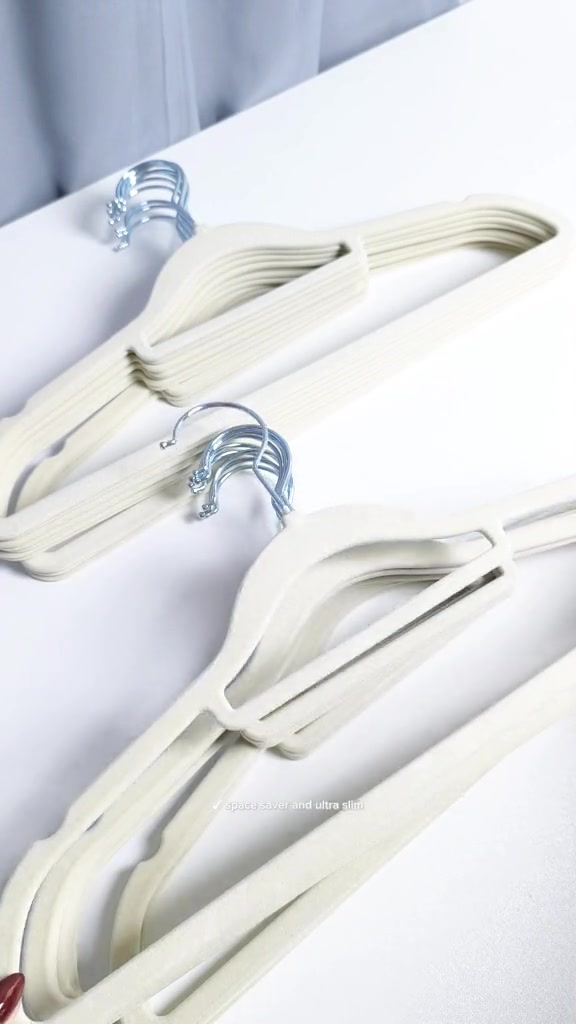 Dua longgokan hanger velvet warna krim terbaring di atas meja putih dengan hook besi menghadap atas