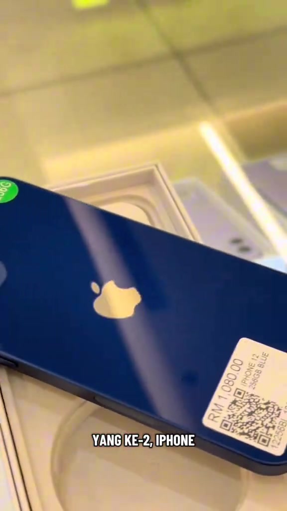 Bahagian belakang iPhone 12 warna biru dengan tag harga kedai bercetak RM1,080.00 beserta keterangan iPhone 12 256GB Blue dan kod QR