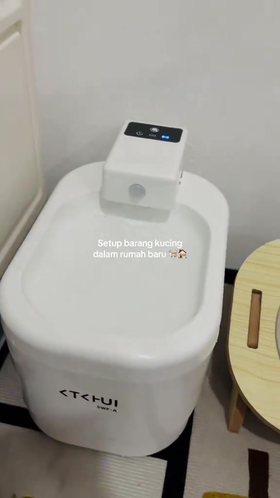 Pancuran air kucing warna putih dengan unit sensor di bahagian atas, diletak di sudut rumah