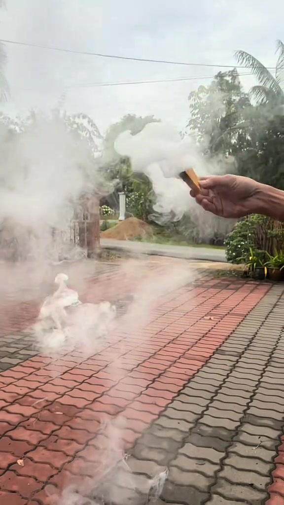 Tangan memegang ubat nyamuk bakar yang sedang mengeluarkan asap tebal di kawasan berturap luar rumah