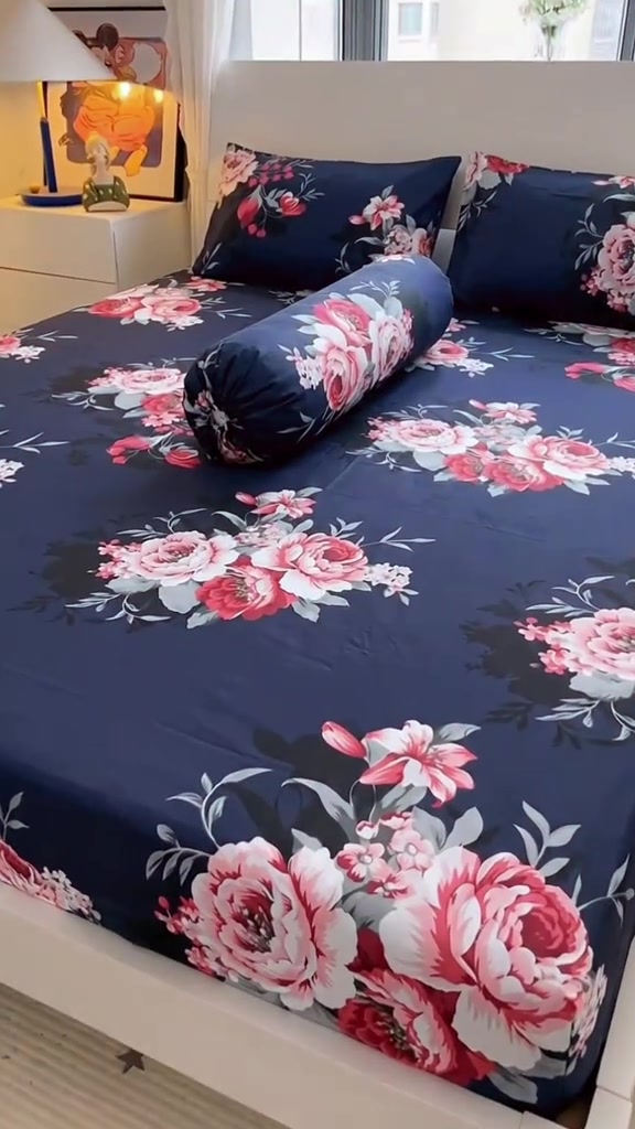 Katil dengan cadar fitted bercorak bunga navy yang kemas bersama dua bantal dan bolster sepadan