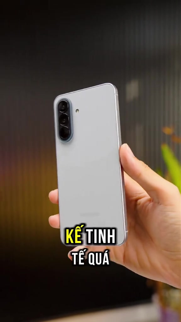 Mặt lưng Galaxy A57 5G màu xám nhạt với cụm ba camera xếp dọc, cầm trên tay