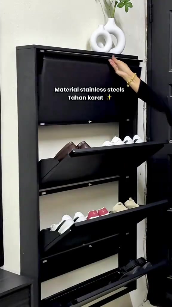 Tangan menutup panel atas rak kasut flip-down stainless steel hitam tergantung dinding dengan kasut di tray terbuka