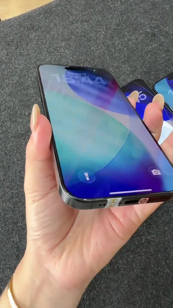 Cạnh dưới của một chiếc iPhone với tem kín còn nguyên, cầm nghiêng trên tay
