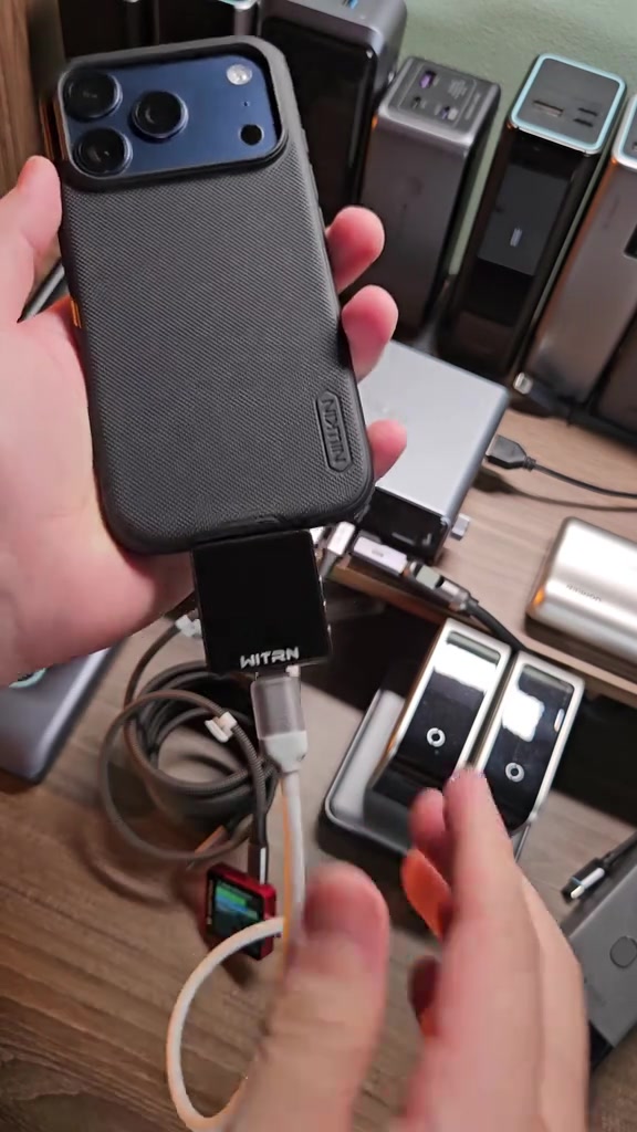 iPhone ốp lưng màu đen cắm vào đầu đo công suất rồi nối cáp xuống viên sạc dự phòng CUKTECH trên bàn thử