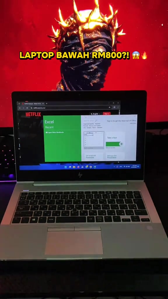Laptop HP EliteBook perak terbuka memaparkan skrin Excel, di hadapan monitor berlatar merah