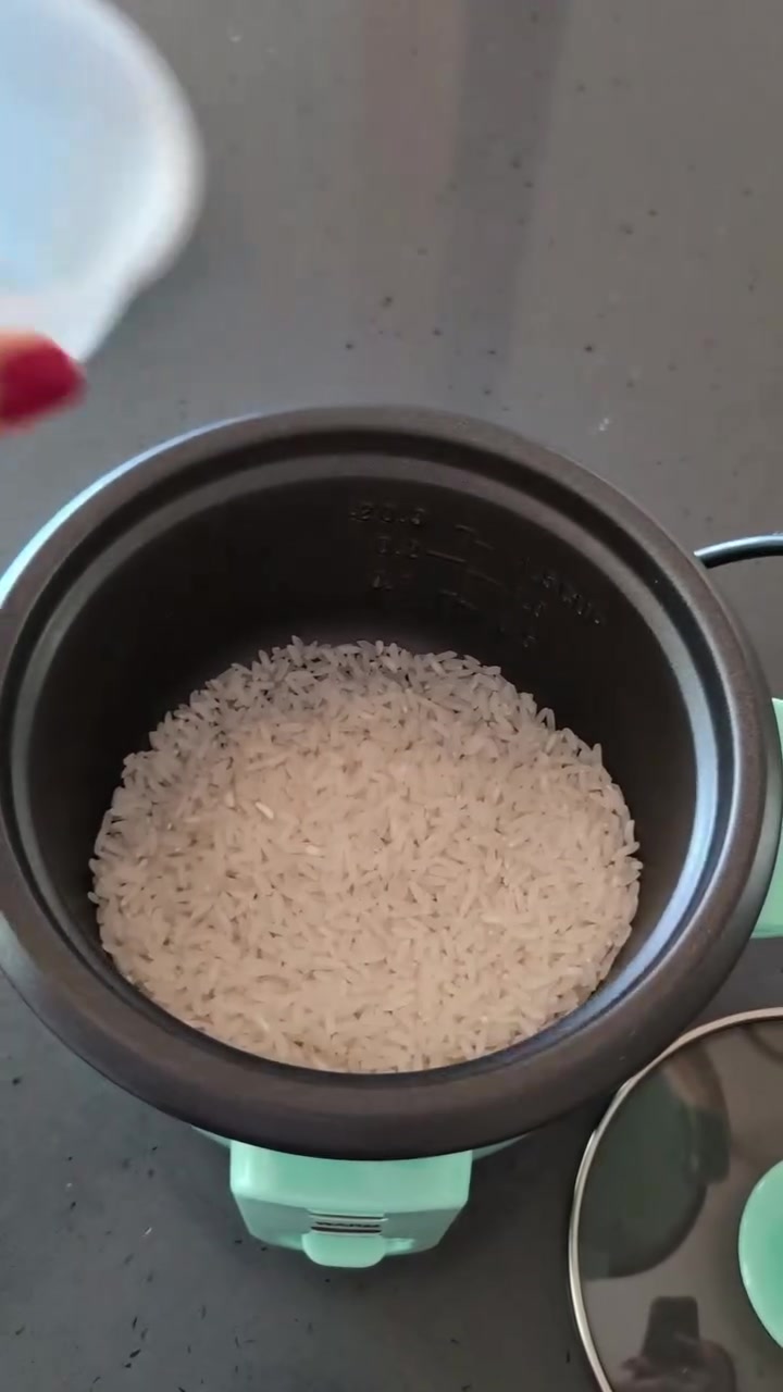 Periuk dalam rice cooker mini berisi beras mentah, dengan garisan sukatan air tertera pada dinding periuk
