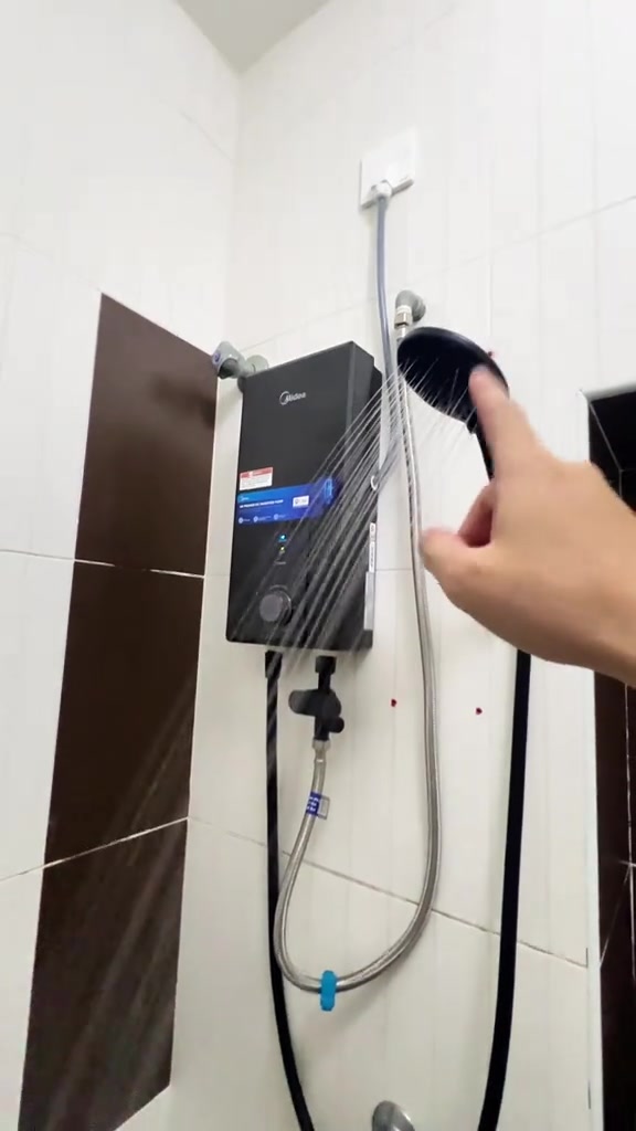 Unit water heater Midea terpasang di dinding jubin putih dengan kepala shower menyembur air
