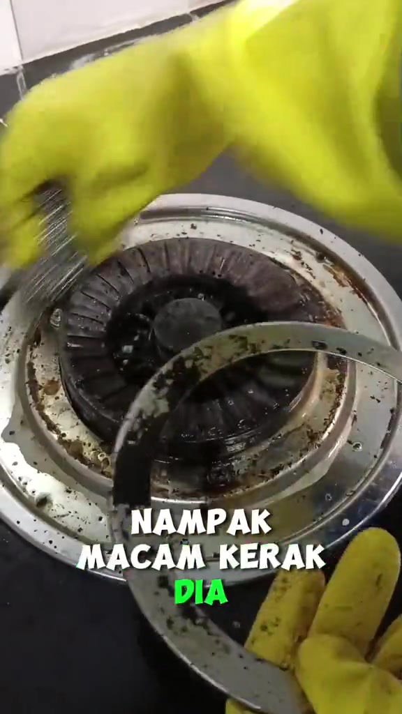 Tangan bersarung tangan getah kuning memberus ring dapur gas dengan berus dawai