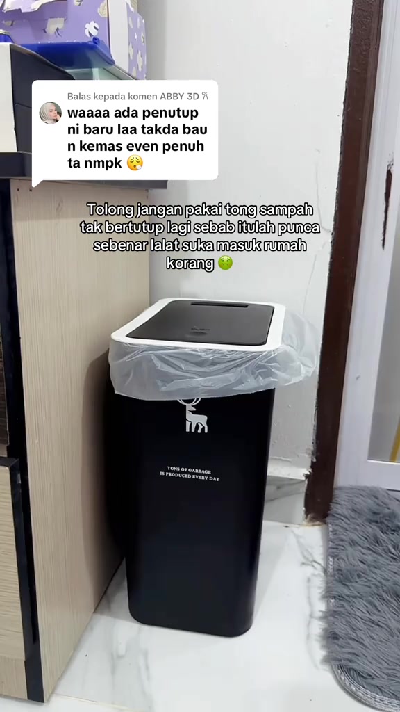 Tong sampah slim hitam bertutup diletakkan di celah sempit antara kabinet dan dinding, beg plastik dilipat di bibir tong